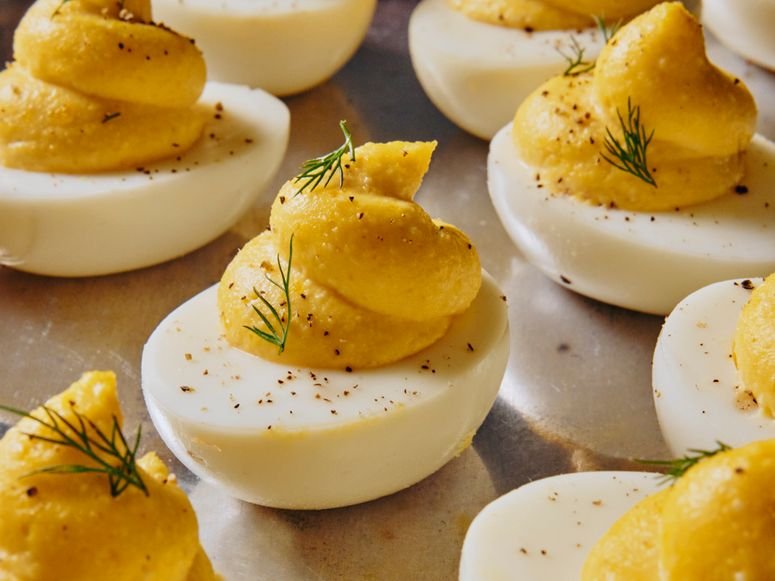 A multitude of deviled eggs garnished generously with pepper and dill sprigs on a reflective silver platter.
